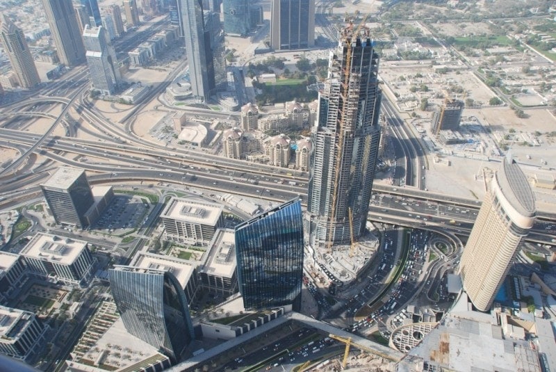 aerial shot looking down at a city centre towards several glass skyscrapers and a large steel tower in construction - What to Eat in Dubai
